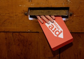 A hand reaching through the letterbox, holding a red Christian Aid envelope.
