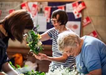 Women making floral arrangements in a church with Christian Aid bunting handing in the background